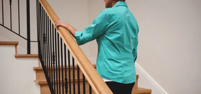 Personne âgé qui monte les marches d'un escalier avec garde corps 